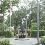 Soldier statue in park with American flags and flowers.