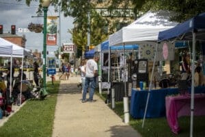 Outdoor street fair with vendor booths and shoppers.