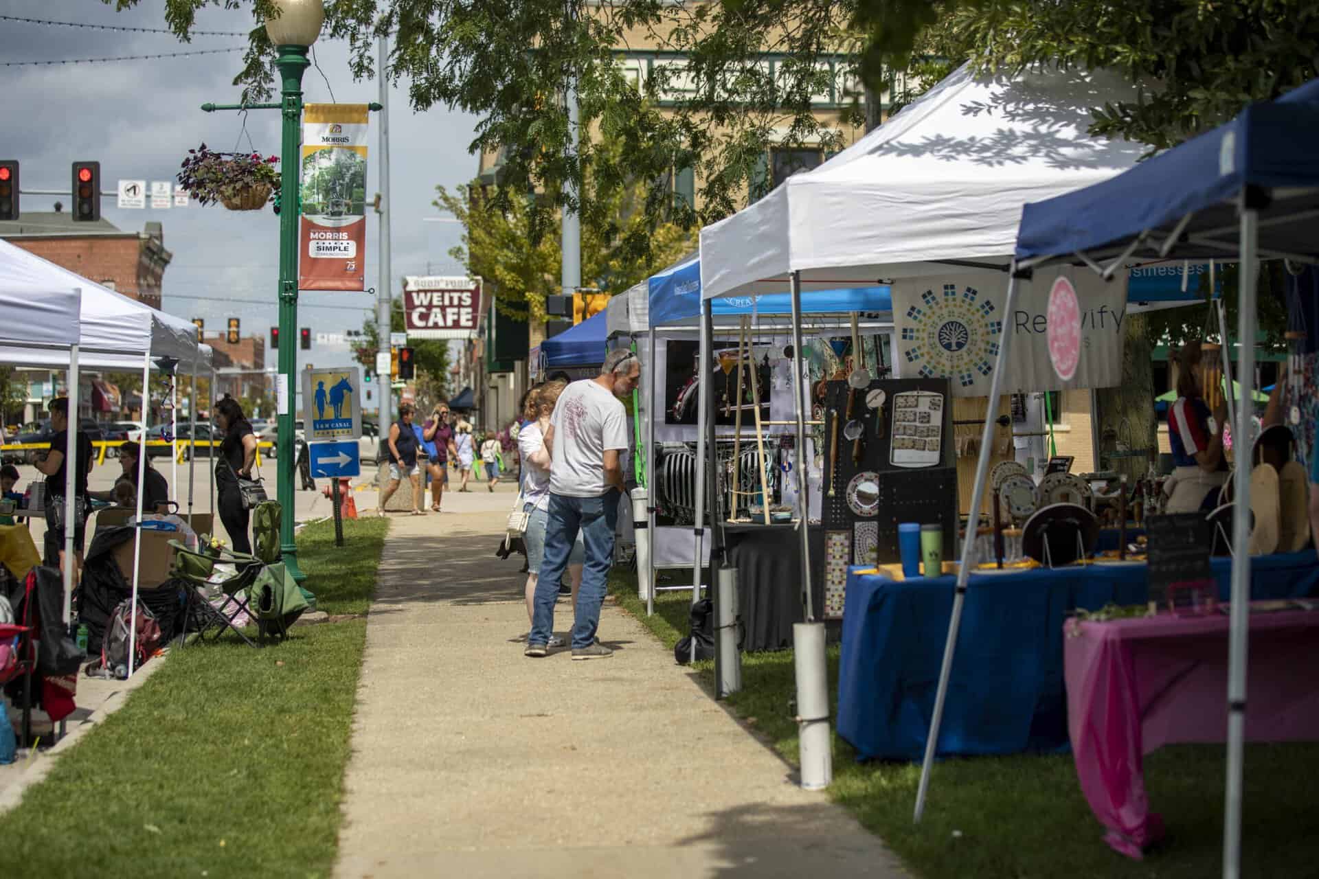 Outdoor street market with shoppers and vendor tents.